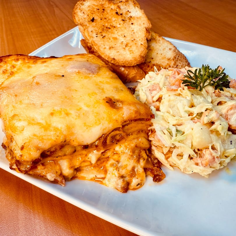 Venezuelan lasagna with melted cheese, a side of coleslaw, and two pieces of garlic bread.