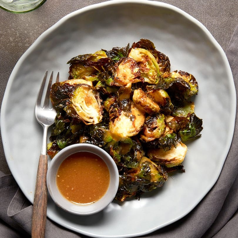A plate of roasted Brussels sprouts with a side of dipping sauce and a fork.